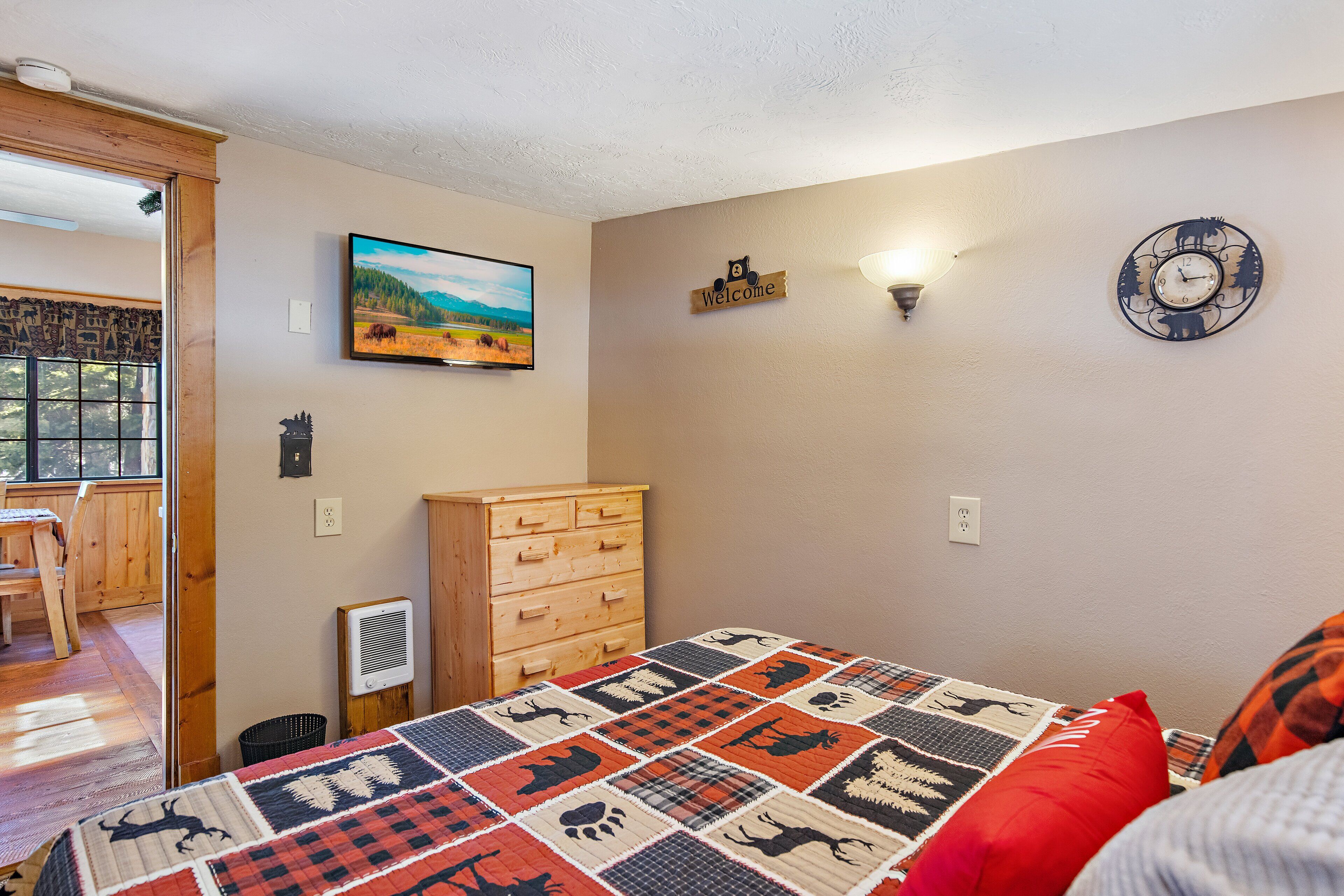 Un dormitorio con colcha acolchada, cómoda de madera, un reloj de pared y un letrero de bienvenida.