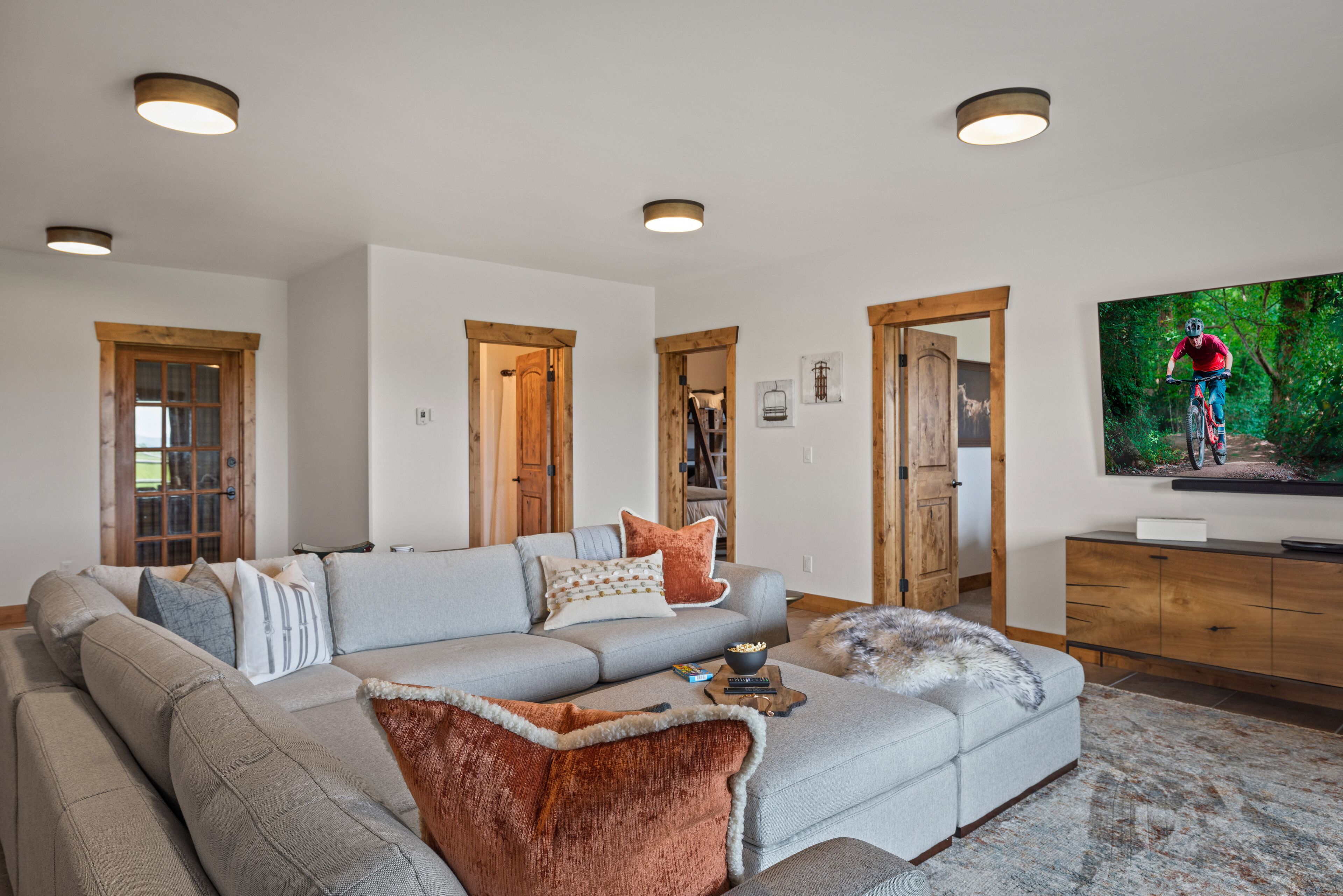 A modern living room with a sectional sofa, wooden doors, a flat-screen TV, and a rustic rug.