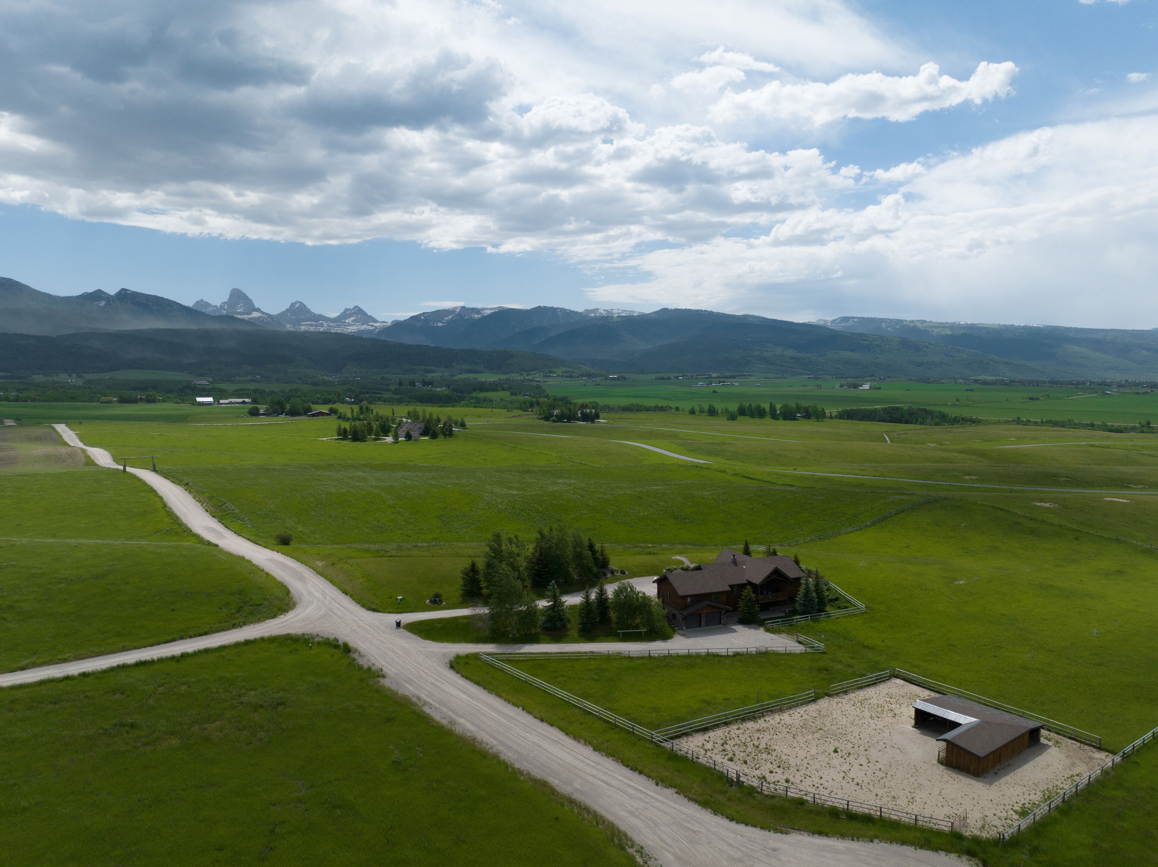 Un paysage rural avec une ferme, des champs verdoyants et des montagnes en arrière-plan.