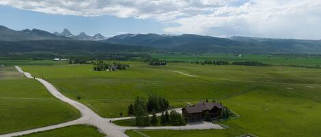 A rural landscape with a farmhouse, green fields, and mountains in the background.