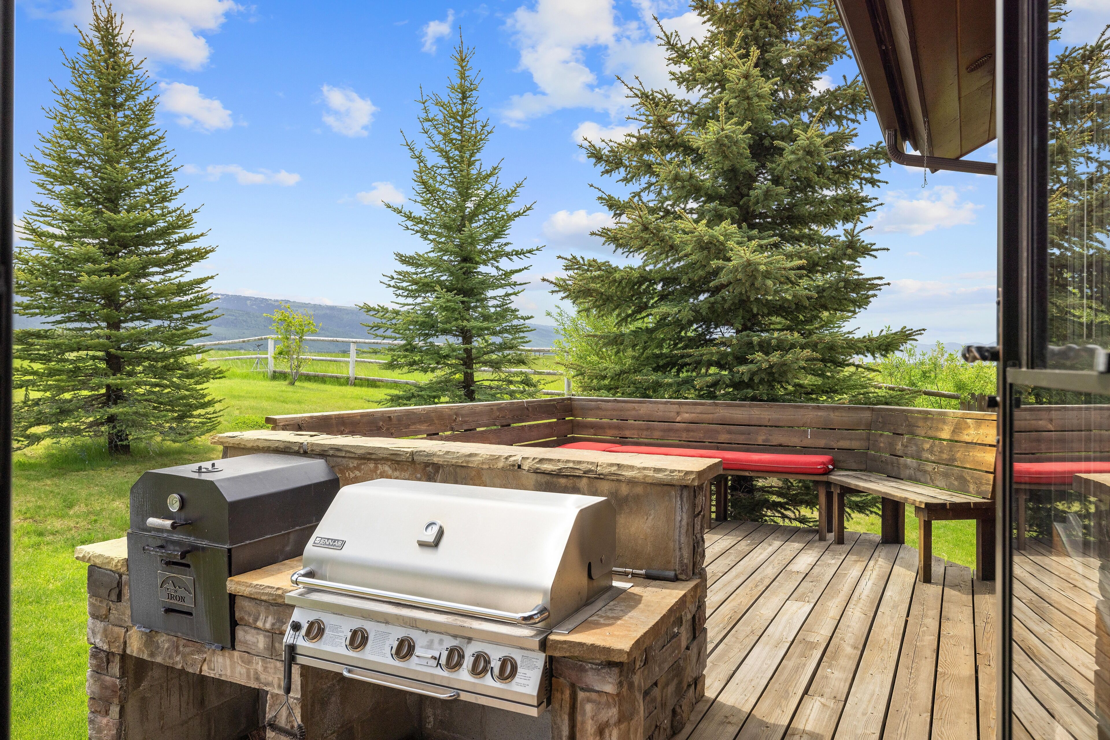 Una terrazza esterna con barbecue, posti a sedere e vista su alberi e montagne.