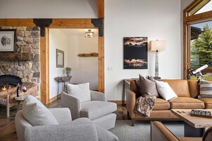 A cozy living room with a stone fireplace, leather sofas, and a large window offering a view of the outdoors.