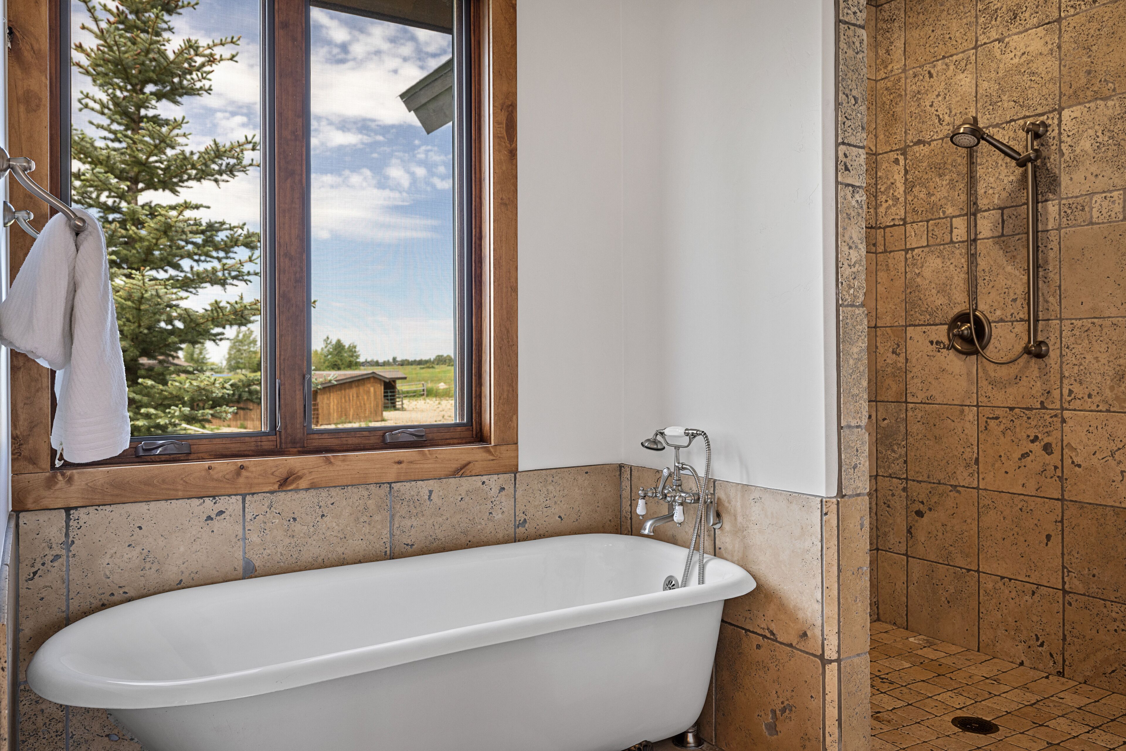 A bathroom with a freestanding bathtub, a window with a towel hanging on the door, and a shower area with a handheld showerhead.