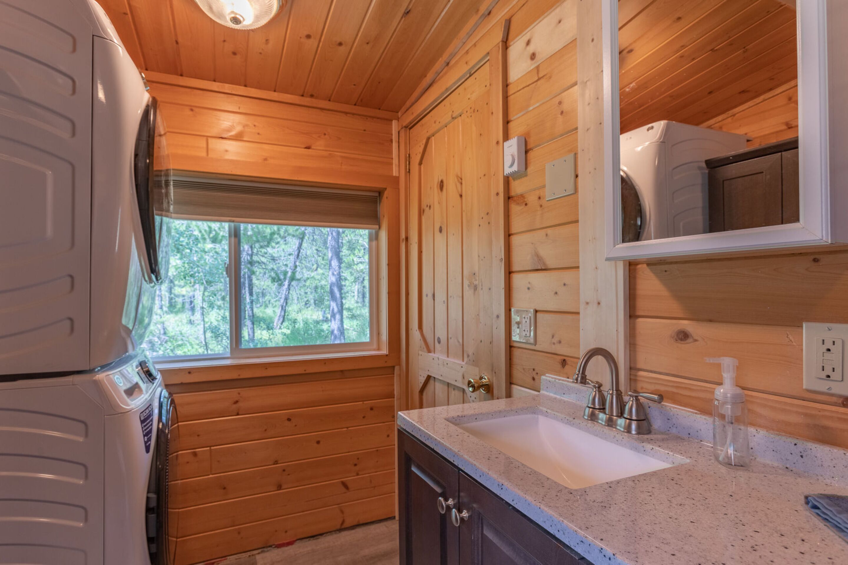 L’intérieur d’une cabane en bois, avec un lave-linge, un évier et une fenêtre donnant sur les arbres.