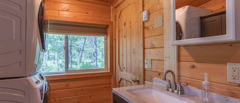 L’intérieur d’une cabane en bois, avec un lave-linge, un évier et une fenêtre donnant sur les arbres.