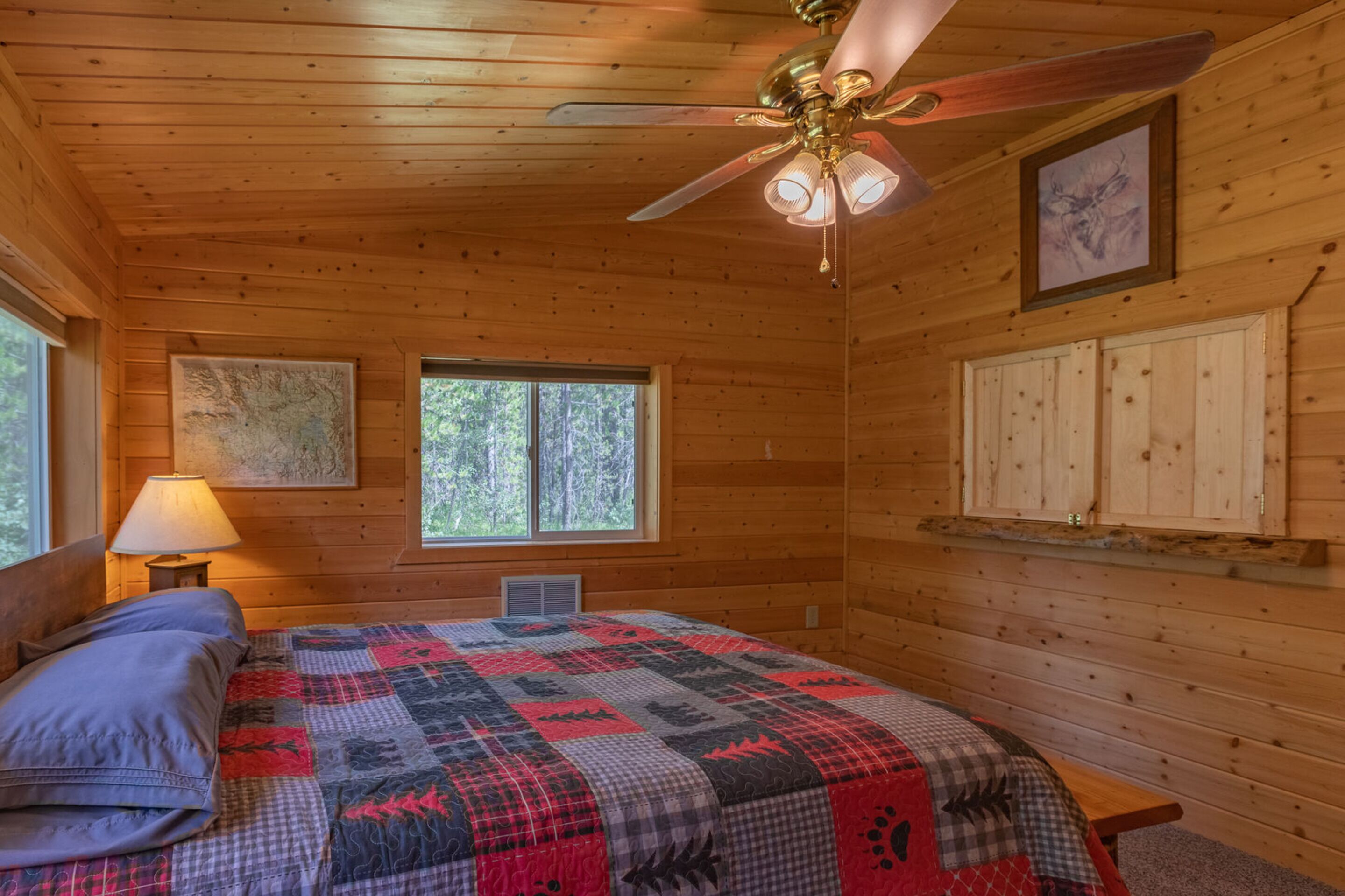 Un dormitorio de cabaña de madera con cama, ventilador de techo, ventana y estante fijado a la pared.