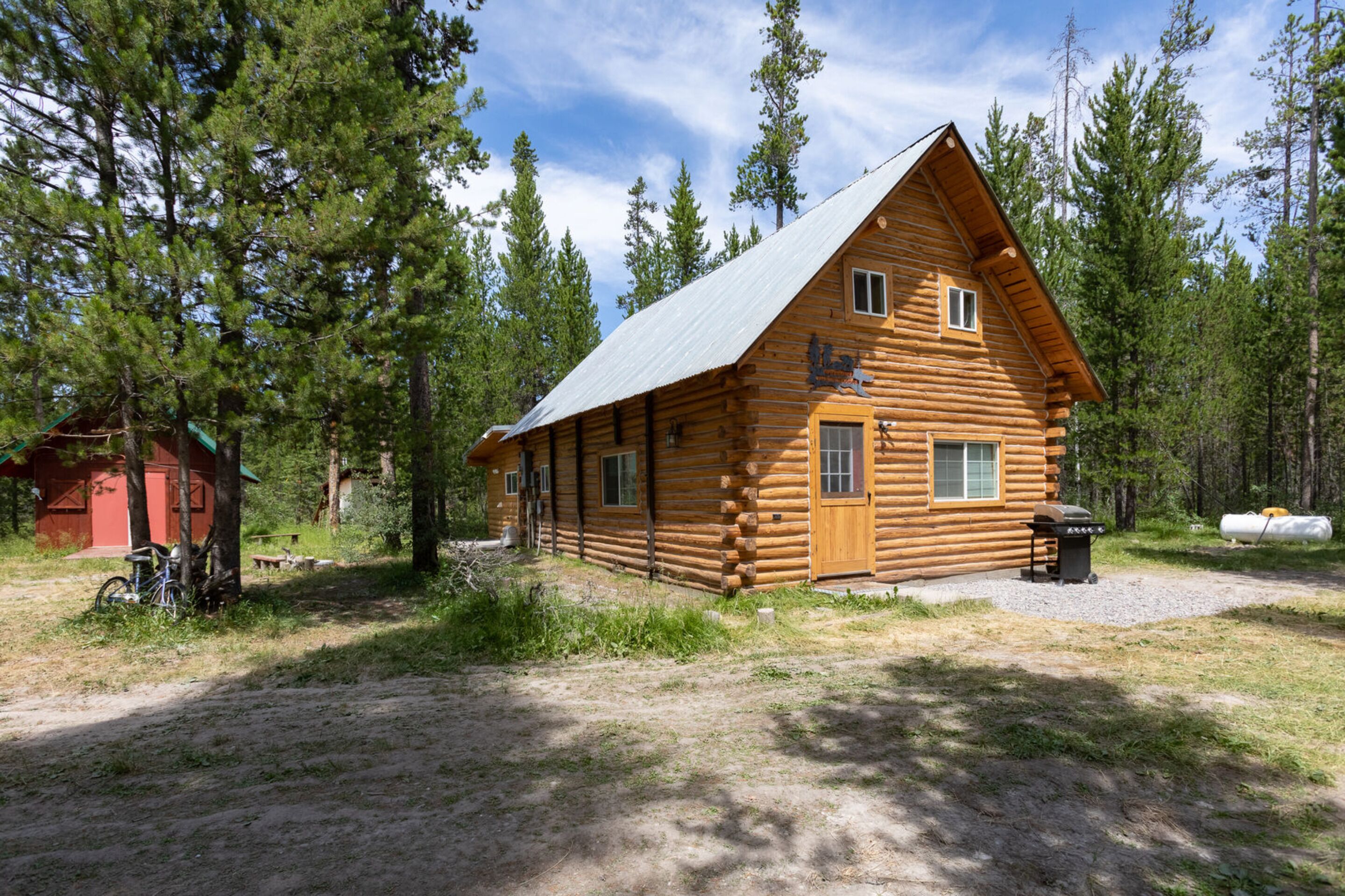 A rustic log cabin with a metal roof, surrounded by trees.