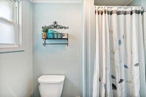 Ein Badezimmer mit Toilette, Ablage für Pflegeprodukte und einer Duschvorhang mit Blättermotiv.