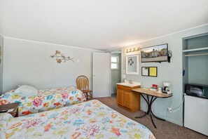 Ein Schlafzimmer mit zwei Betten, einem Holzstuhl, einem kleinen Schreibtisch mit Spiegel und einem Fernseher.