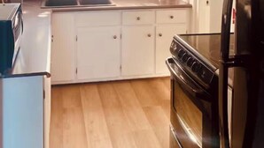 A kitchen with a black stove, white cabinets, a window, and a ceiling fan.