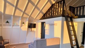 A loft-style room with a high ceiling, a staircase, a grey sofa, and a flat-screen TV.