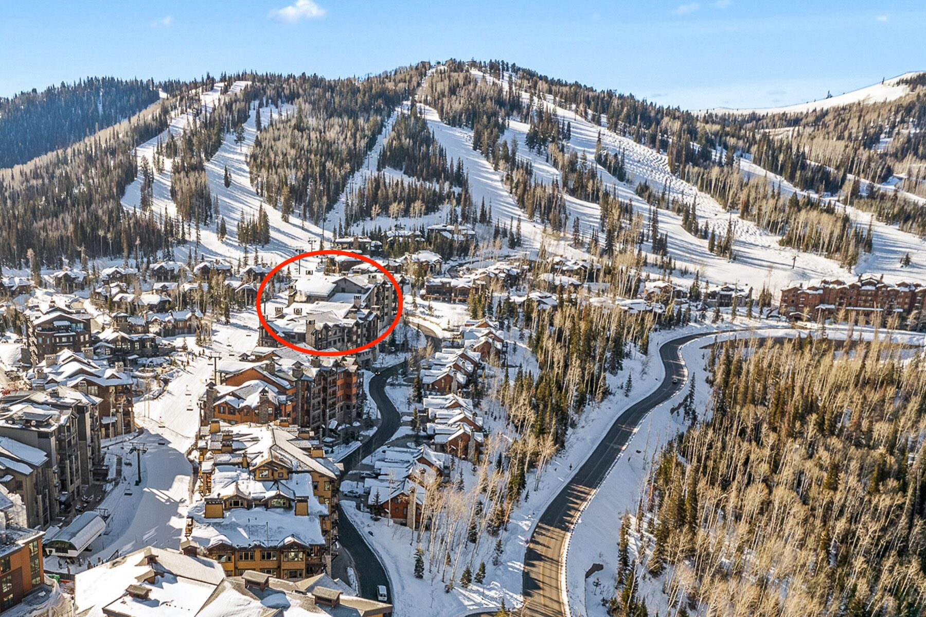 A ski resort with multiple buildings, a winding road, and a snow-covered mountain backdrop.