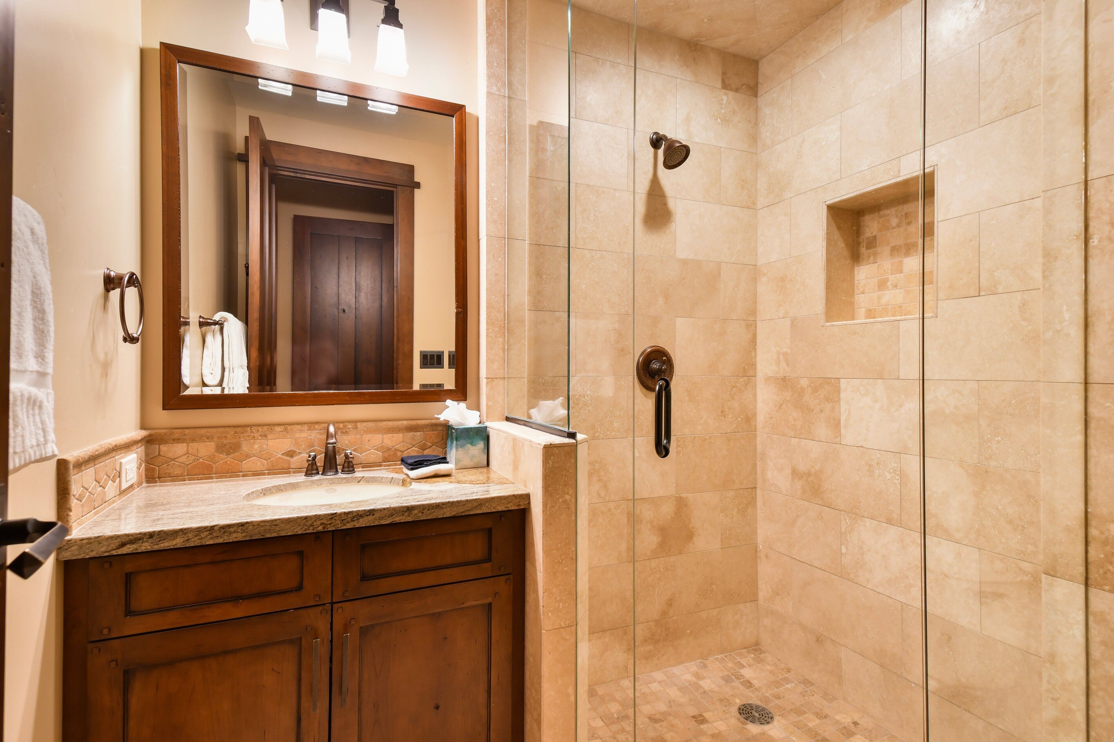 Une salle de bain dotée d’une douche à parois de verre, d’un meuble-lavabo en bois et d’un grand miroir.