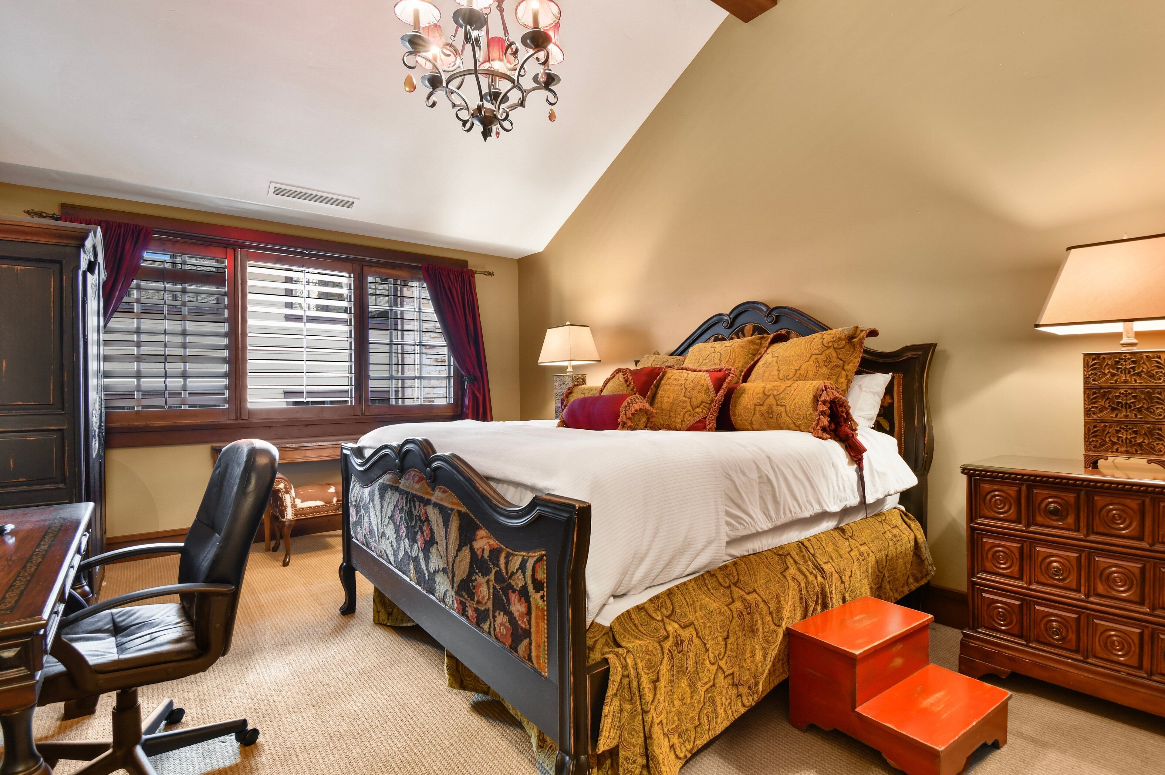 A bedroom with a large bed, a desk, a chair, a dresser, and a window with blinds.