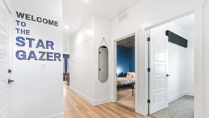 A hallway with a 'Welcome to the Star Gazor' sign, wooden flooring, a mirror, a bed with a blue wall, and a starry night decoration. - The Stargazer in Boise (Garden City)