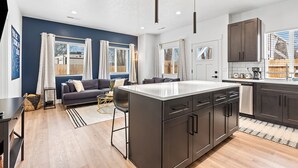 A modern kitchen with a central island, dark cabinetry, and a dining area with a sofa. - The Stargazer in Boise (Garden City)