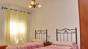 Et soveværelse med to enkeltsenge, et natbord med lampe, en lysekrone og et vindue med gardiner.