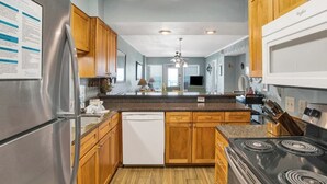A modern kitchen with wooden cabinets, a stainless steel refrigerator, a dishwasher, and a black stove. - Steps Away from the Beach, Food, and Entertainment (Gulf Shores)