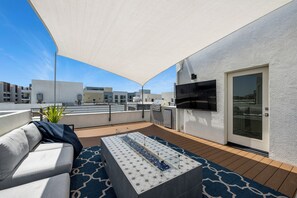 A rooftop terrace with a sofa, a tiled coffee table, a grill, and a TV mounted on the wall. - Luxury 4 Bed / 3.5 Bath Townhome near Sports/CHOC/Disneyland/Chapman/Beach (Anaheim)