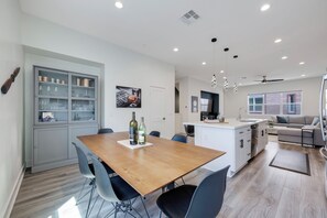 A modern kitchen with a central island, dining table with chairs, and a built-in cabinet with glass doors. - Luxury 4 Bed / 3.5 Bath Townhome near Sports/CHOC/Disneyland/Chapman/Beach (Anaheim)