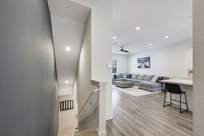 A modern living room with a grey sofa, a coffee table, and a dining area with a white table and black chairs. - Luxury 4 Bed / 3.5 Bath Townhome near Sports/CHOC/Disneyland/Chapman/Beach (Anaheim)