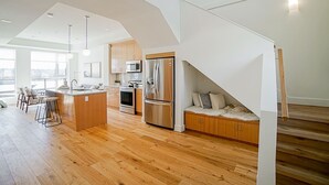 A modern kitchen with wooden flooring, a central island, stainless steel appliances, and a seating area with a cushioned bench. - Delux River View Home 2beds (New Westminster)