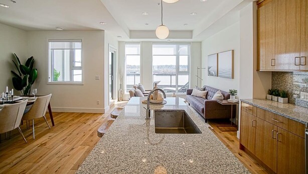 A modern kitchen with granite countertops, wooden cabinets, and a large island with a sink. - Delux River View Home 2beds (New Westminster)