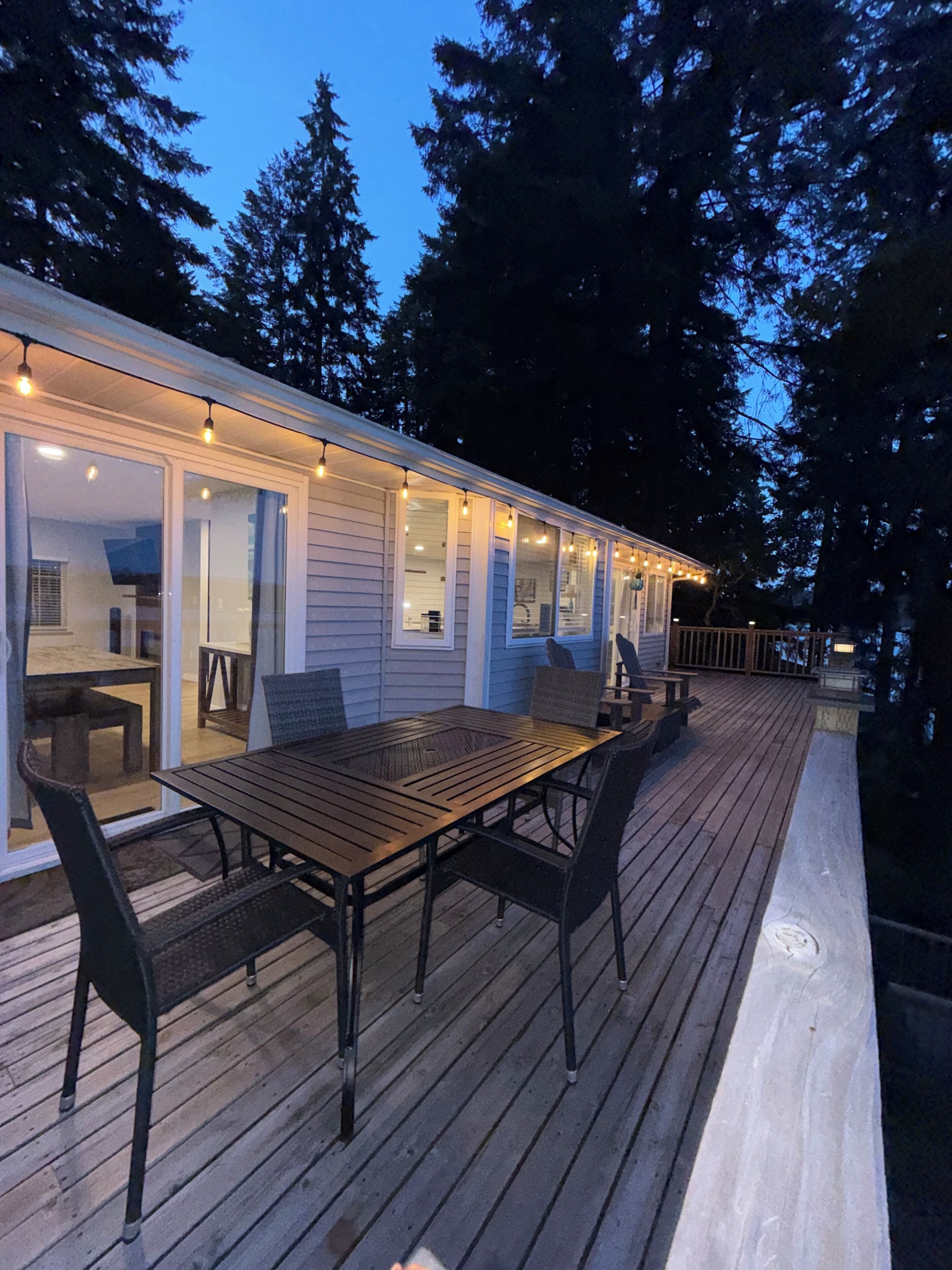 A wooden deck with a dining table and chairs, surrounded by glass doors leading to a room.