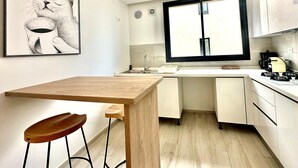 A modern kitchen with a wooden table, bar stools, a large window, and a framed artwork of a cat. - A12 Stylish and Modern 2bds in La Marsa (La Marsa)