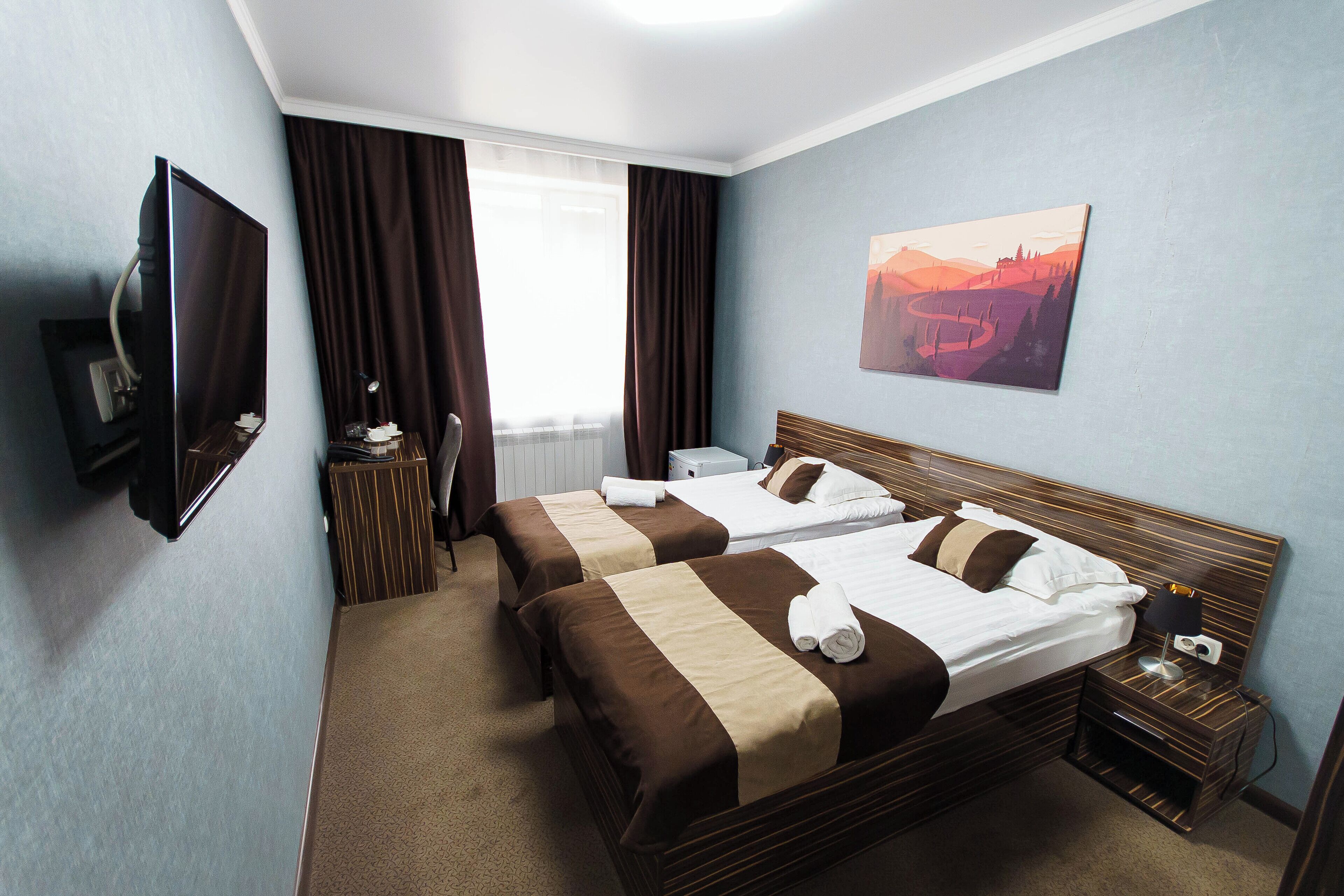 Habitación de hotel con dos camas, un televisor, un cuadro y un escritorio con una lámpara.
