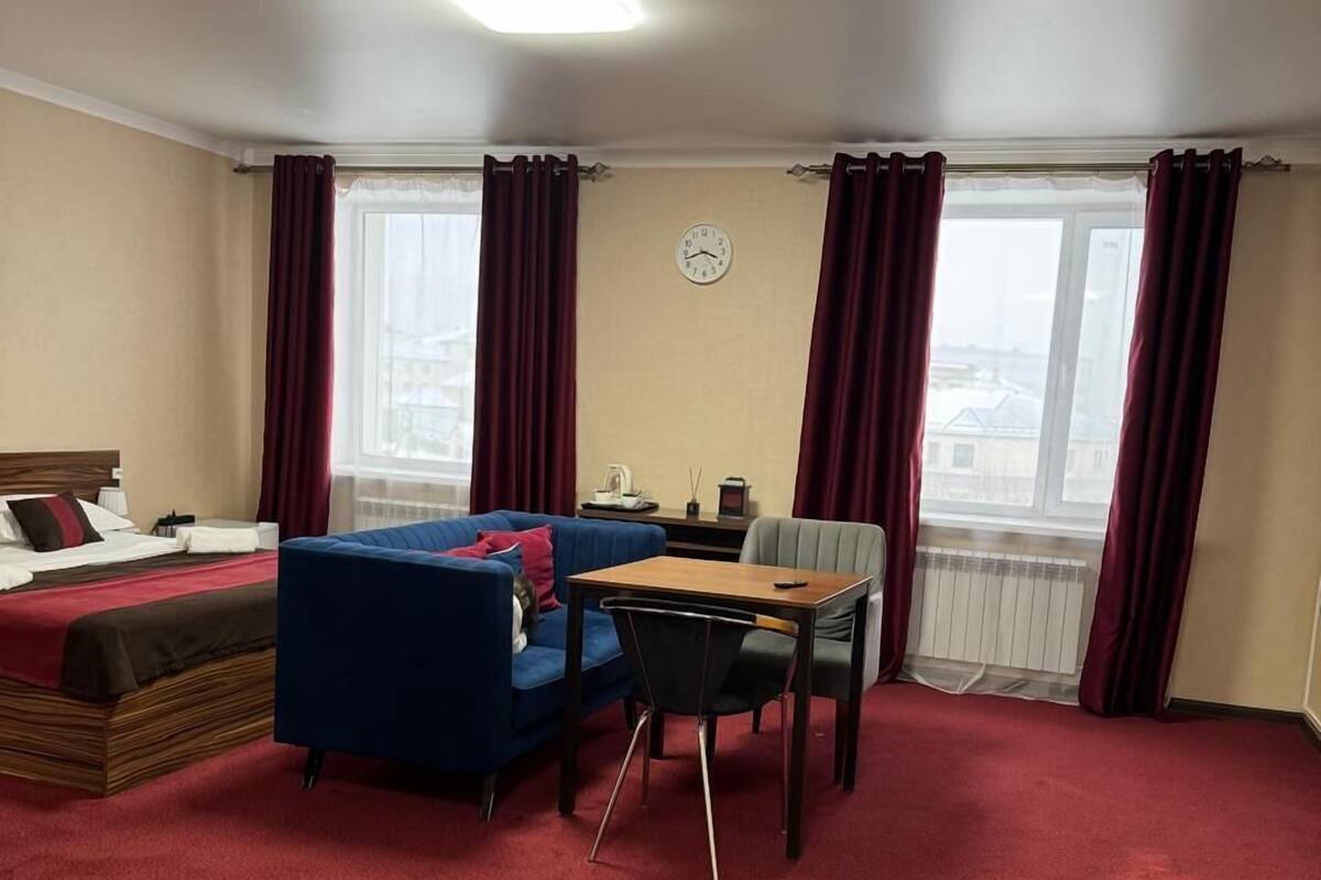 Une chambre d’hôtel avec un lit, un canapé bleu, une table en bois et une moquette rouge.