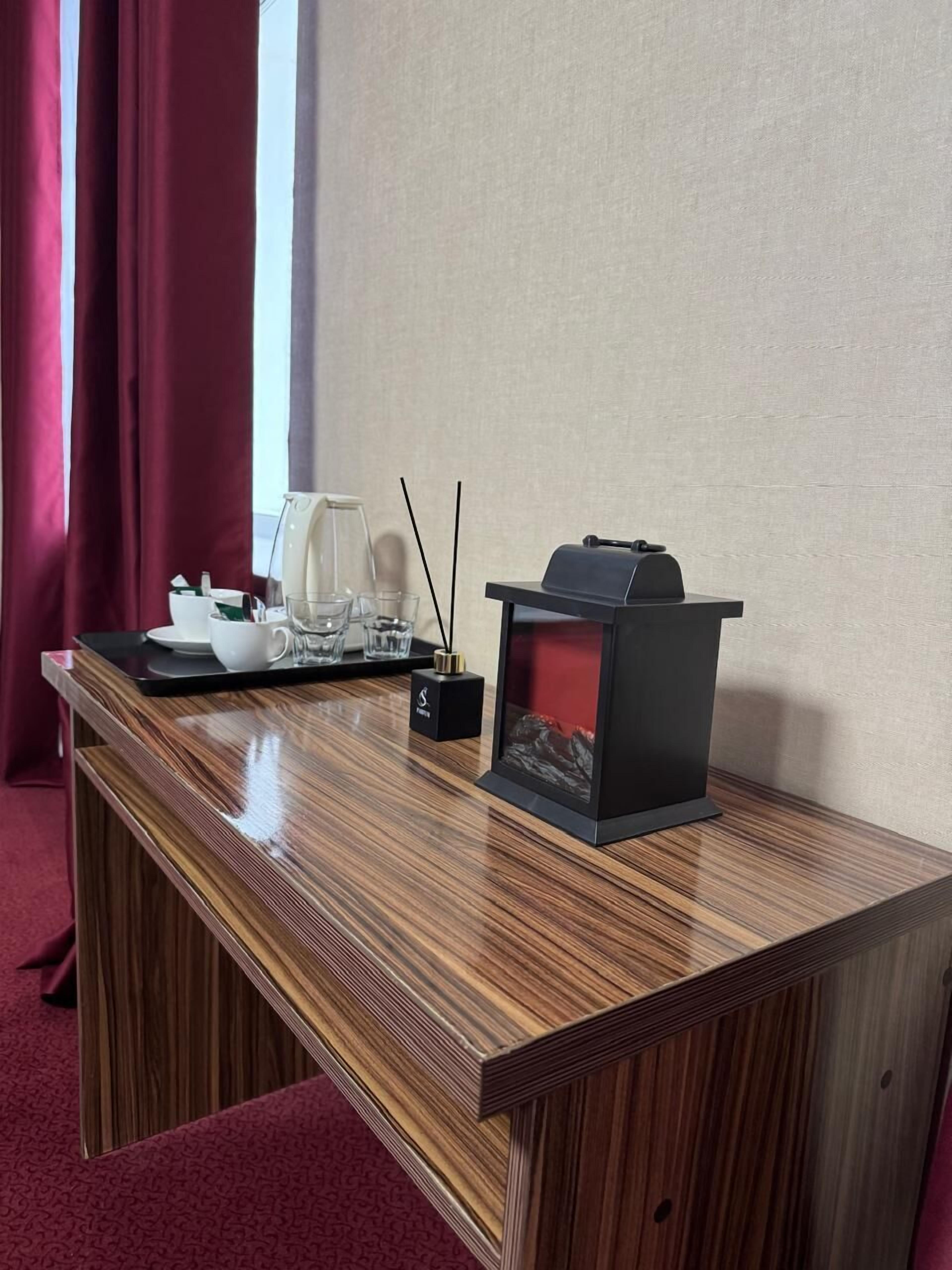 Een houten bureau met een zwarte speaker, een witte waterkoker en een klein zwart kastje met een logo.
