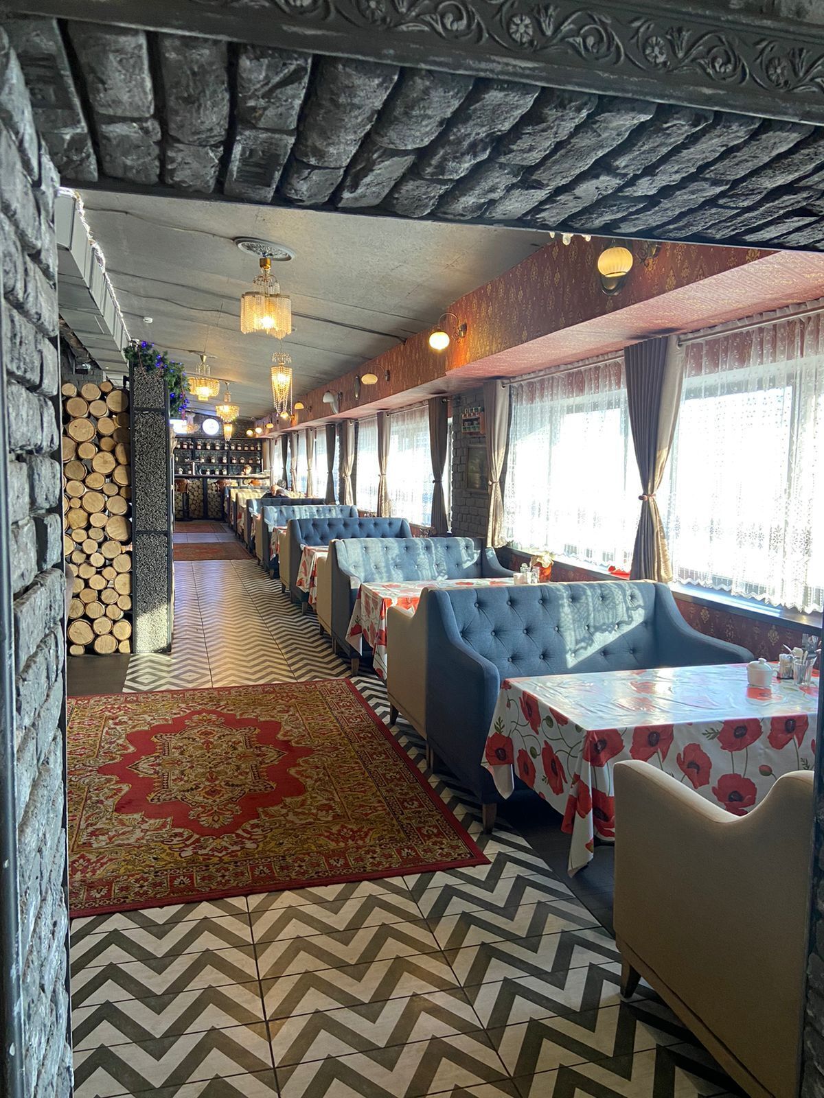 Un ristorante con un lungo bancone, sedute imbottite blu, piastrelle a pavimento decorate e un muro decorativo con legna impilata.