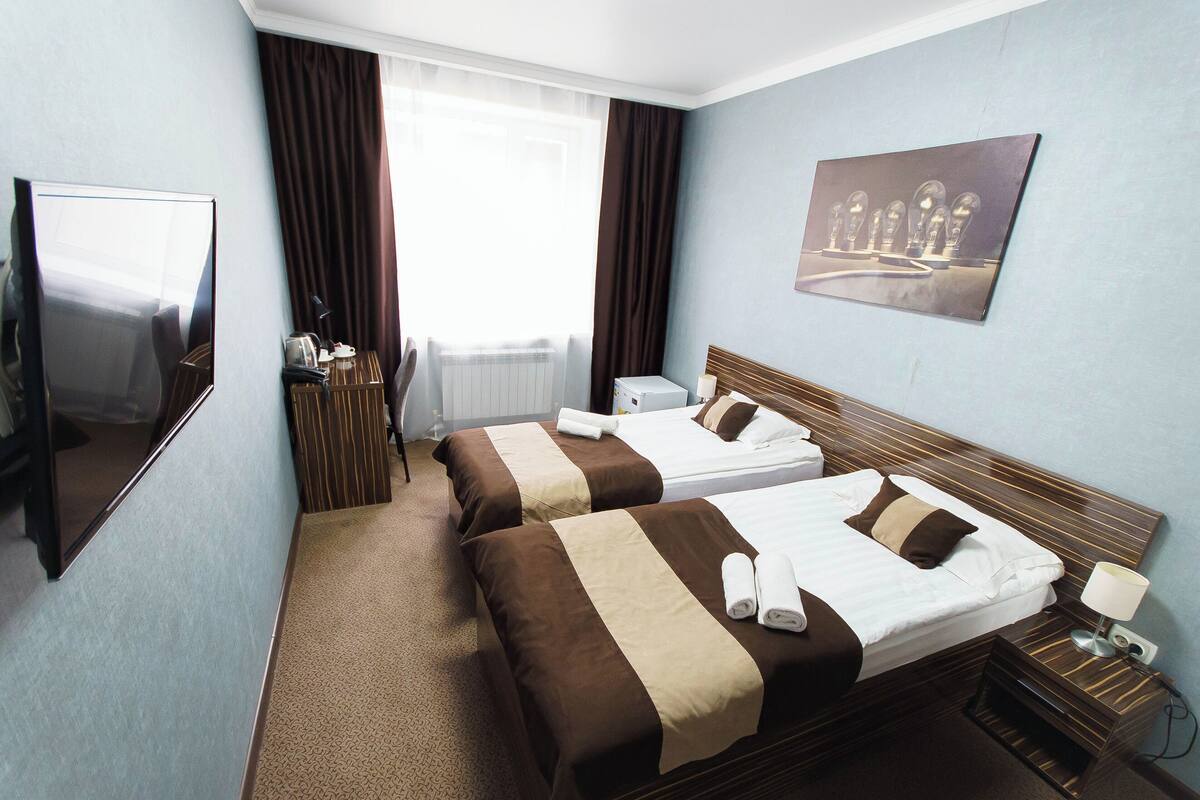 Une chambre d’hôtel avec deux lits, une télévision, une fenêtre avec des rideaux et un tableau au mur.