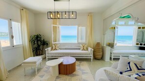 Una habitación con vista al mar, un sofá blanco, una mesa redonda y un sillón blanco.