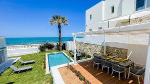 Zona de piscina con vista al mar, una mesa de comedor con sillas y una palmera.