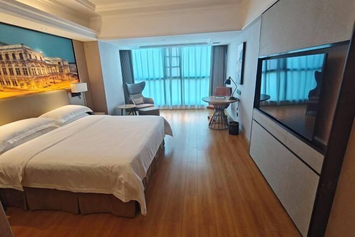 Habitación de hotel con una cama grande, un escritorio, una silla, un televisor y vistas a la ciudad desde la ventana.