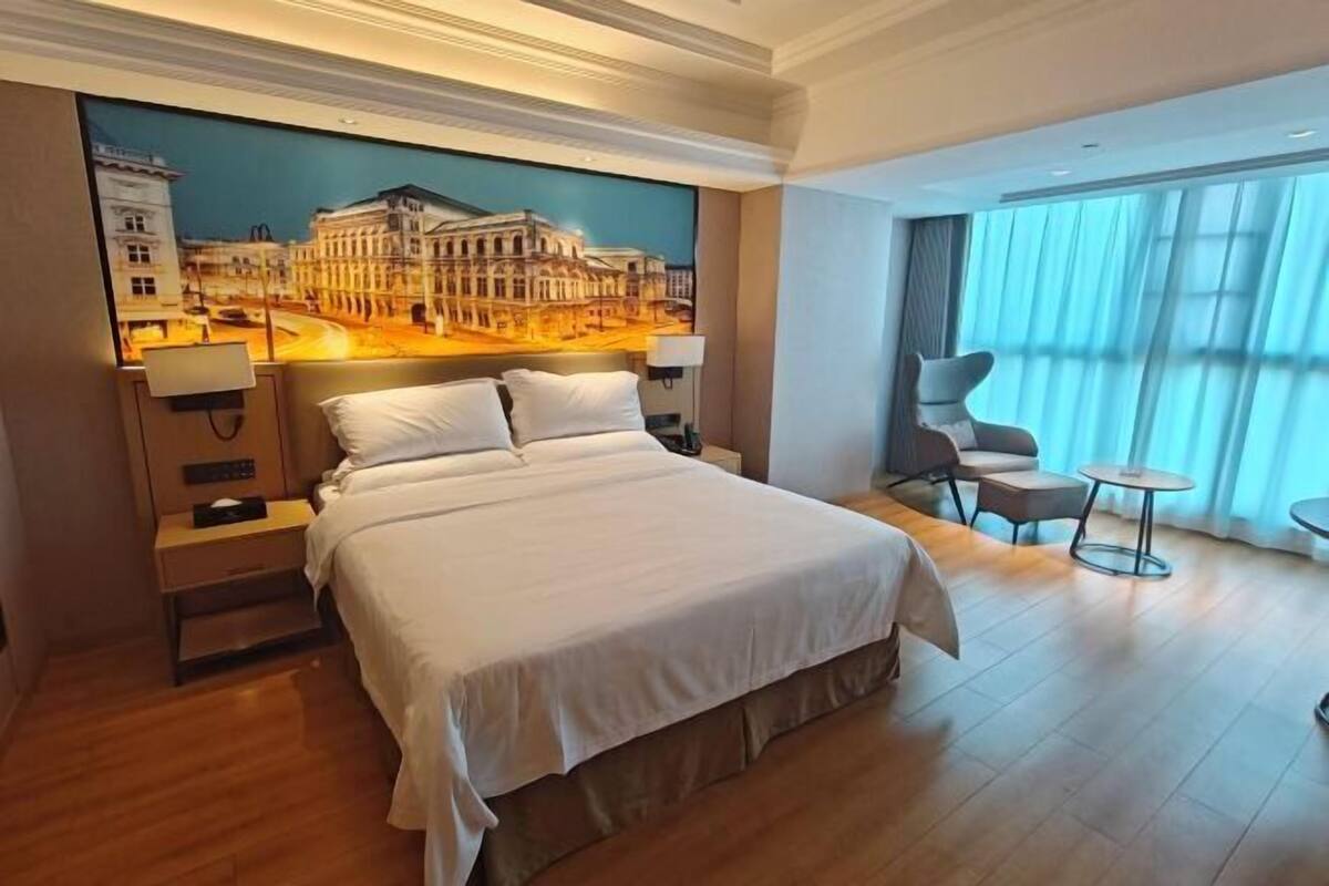Habitación de hotel con una cama grande, una mesita de noche, un escritorio, una silla y vistas a un paisaje urbano por la ventana.