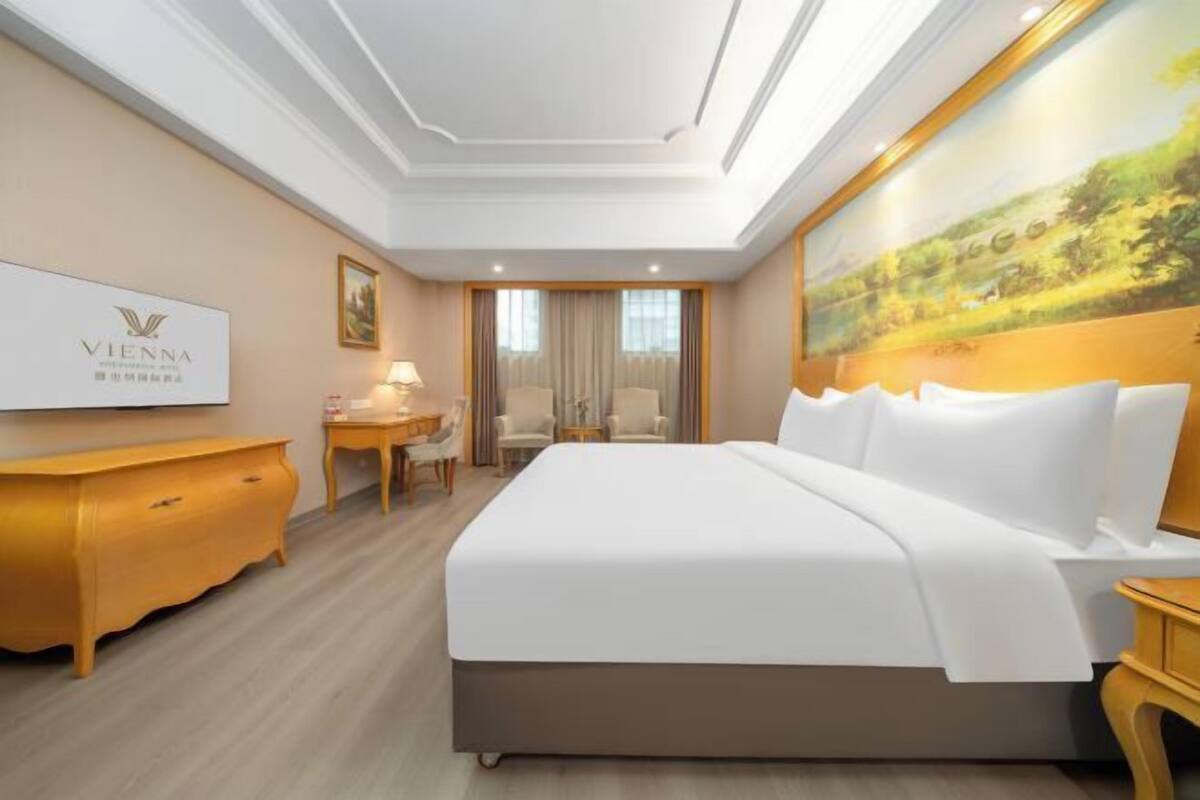 Una habitación de hotel con una cama grande, un escritorio, una silla, un televisor y un cuadro en la pared.