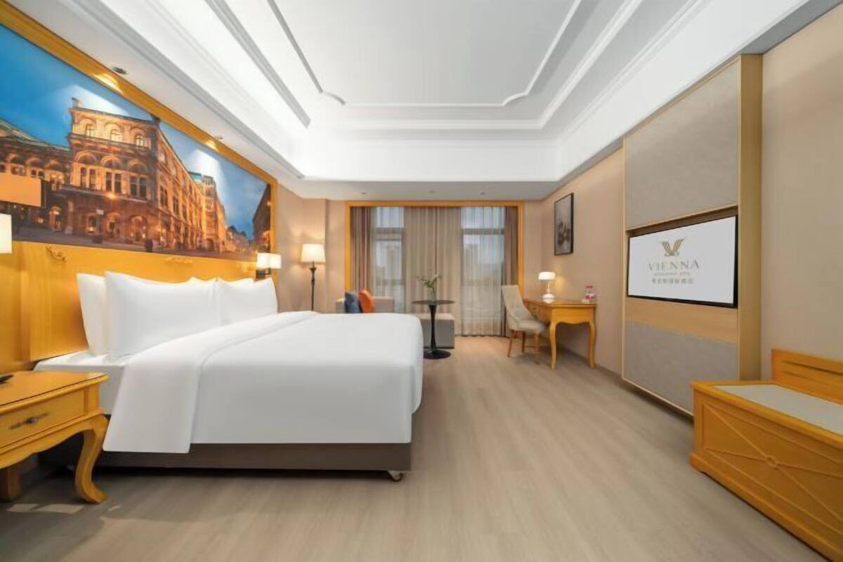 Una habitación de hotel con una cama grande, un escritorio, una silla, una mesita y un cuadro en la pared.