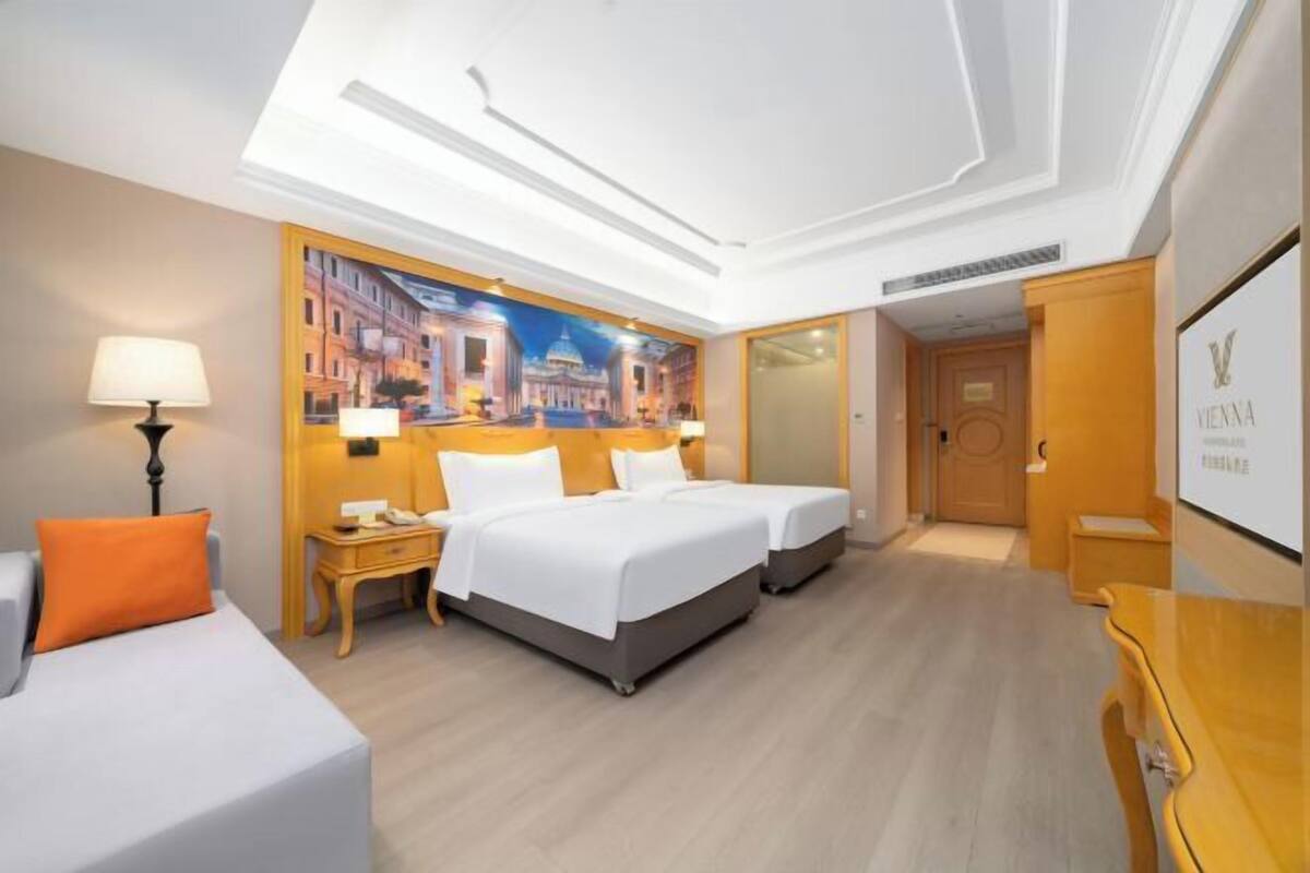 Una habitación de hotel con dos camas, un escritorio, una silla, una lámpara y un cuadro en la pared.