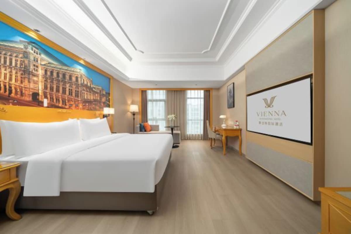 Ein Hotelzimmer mit einem großen Bett, einem Schreibtisch, einem Stuhl, einer Lampe und einem Bild an der Wand.