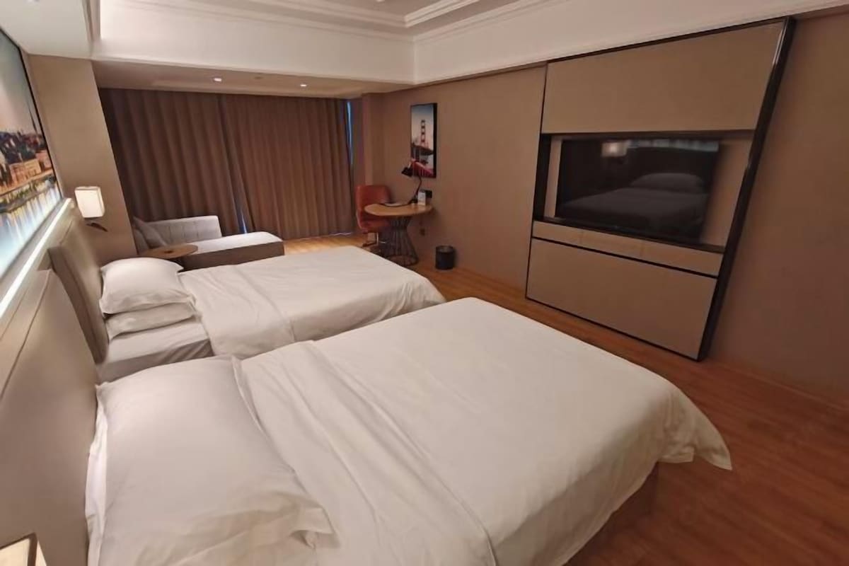 A hotel room with two beds, a TV, a desk, and a chair.