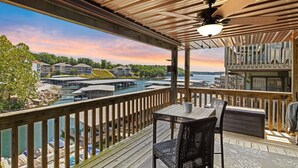 Een overdekt terras met een tafel en stoelen, met uitzicht op een jachthaven met boten en gebouwen.