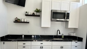 A modern kitchen with white cabinets, a black countertop, a built-in microwave, and a coffee maker. - Cozy, Quaint and Sophisticated Loft Style Tiny Home!  (Flagstaff)
