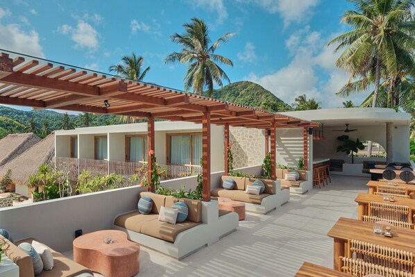 Terraza en la azotea con mobiliario exterior y una pérgola, rodeada de palmeras y montañas al fondo.
