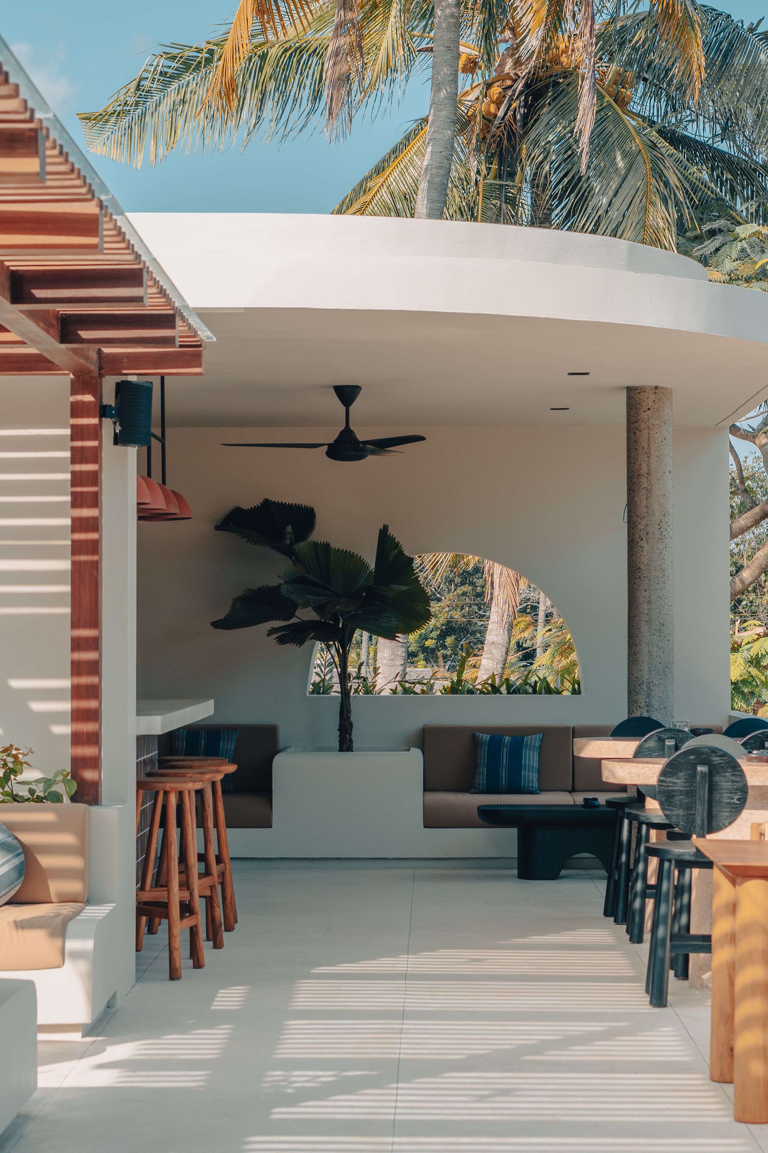 A covered outdoor seating area with a ceiling fan, wooden stools, and a sofa.