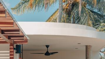 A covered outdoor seating area with a ceiling fan, wooden stools, and a sofa.