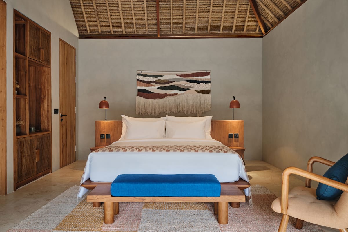Une chambre à coucher comprenant un lit, des lampes de chevet, un banc, une chaise et une décoration murale.