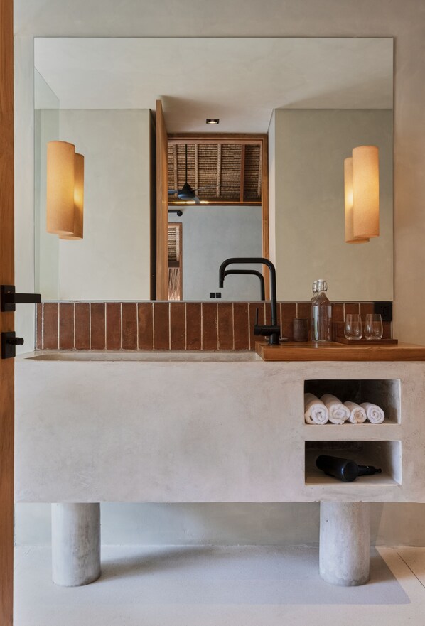 A modern bathroom with a large mirror, two wall-mounted lights, a black faucet, and a towel rack with neatly rolled towels.